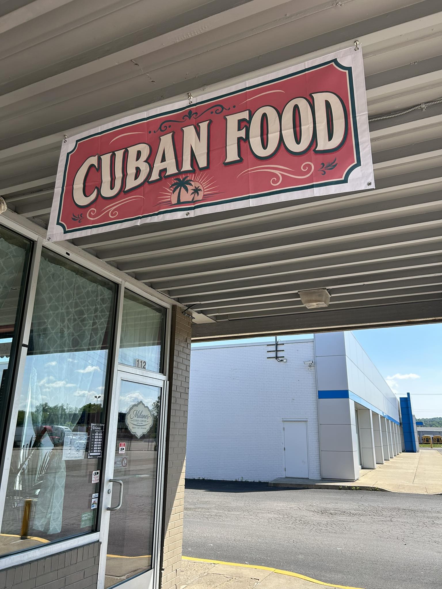 Vintage CUBAN FOOD banner above the Milanes Cuban Corner storefront at 112, with the Milanes emblem on the door